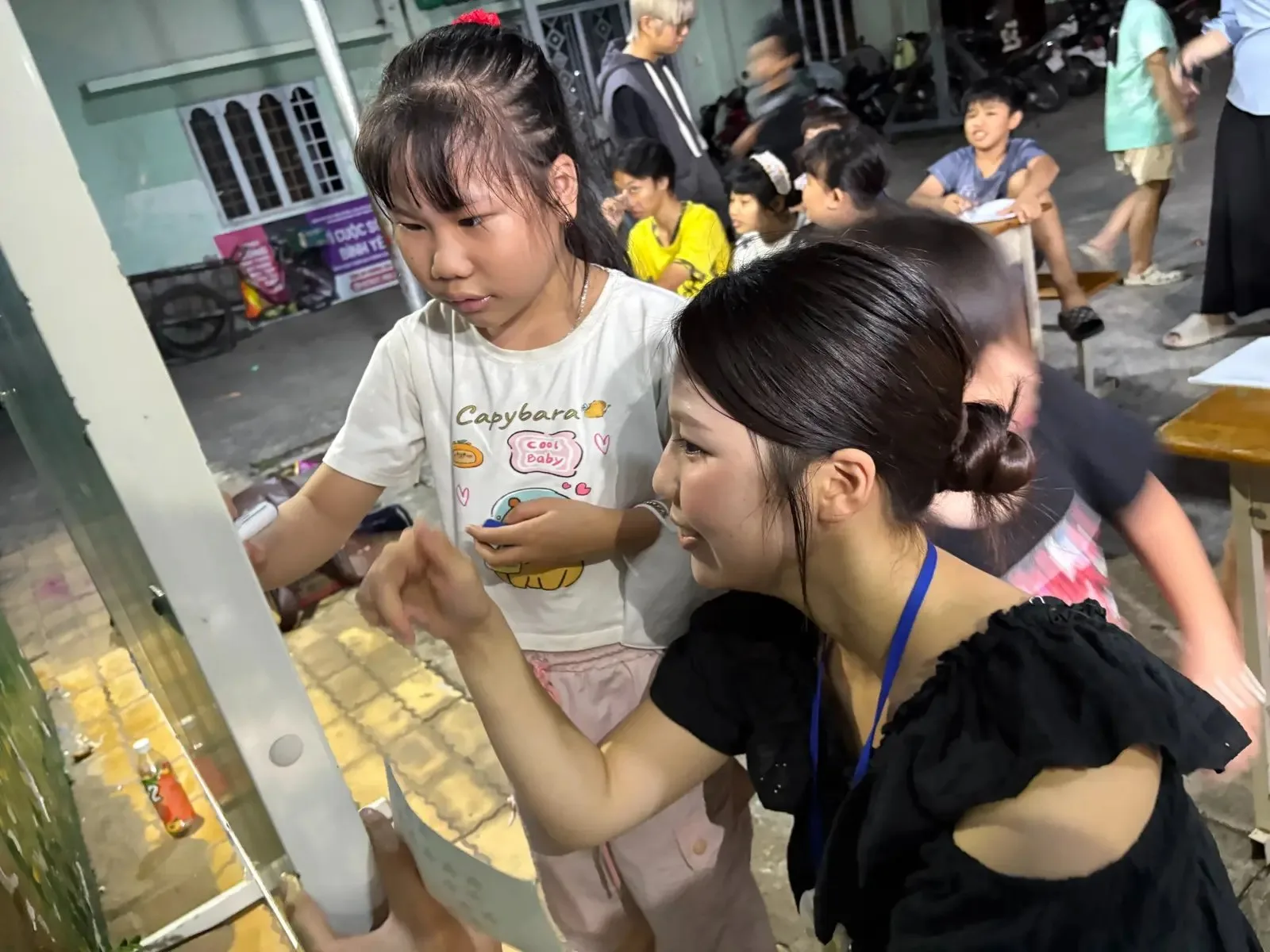ホーチミンの夜の路上で、子どもと一緒に紙に書き込む参加者